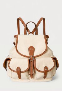 Kangaskangaskassi kermansävyisenä ja ruskein nahkakoristein, jossa on läppäkiinnitys, säädettävät hihnat ja kaksi etutaskua, joissa on läppäkiinnikkeet.