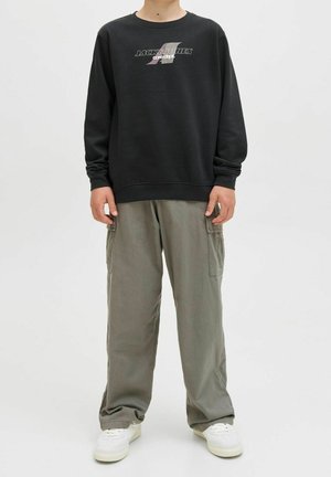 Schwarzer Pullover mit Logo auf der Brust, kombiniert mit lockeren, hellgrünen Cargo-Hosen und weißen Turnschuhen, ausgestattet mit Seitentaschen und entspanntem Schnitt.