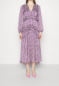 Robe longue à motif floral violet avec un décolleté en V, des manches bouffantes et une taille froncée. Associée à des escarpins roses à bout pointu.