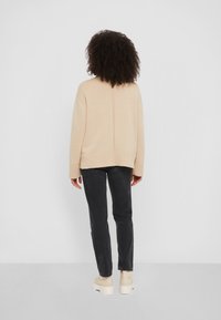 Pull en maille beige à coupe décontractée, avec poignets et ourlet côtelés, porté avec un jean foncé et des chaussures à plateforme, vu de dos.