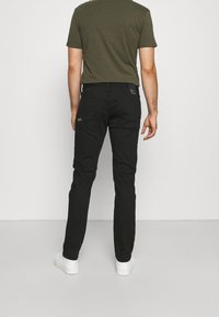 Jeans neri con una vestibilità slim, dotati di una tasca posteriore e passanti per cintura. Abbinati a una camicia verde a maniche corte e scarpe da ginnastica bianche.