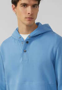 Lichtblauwe hoodie van geweven stof, met een trekkoordcapuchon, knoopsluiting en zichtbare naaddetails. Eenvoudig en casual ontwerp.