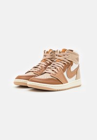 Vysoké tenisky vyrobené z hnědé a krémové kůže s perforovanou špičkou, béžovými akcenty a podpisovým logem na boku. Texturovaná gumová podrážka.