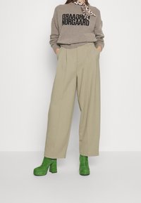 Lichtbeige wijde broek, grijze trui met zwarte tekst, en groene hielbootjes tot de enkel. Inclusief een sjaal met luipaardprint die om de nek is geknoopt.