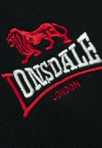 Sort stof med et broderet design af en rød løve over den hvide tekst "ONSDALE" og med små røde "LONDON" nedenfor.