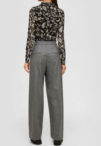 Durchsichtige schwarze Bluse mit abstraktem Blumenmuster, kombiniert mit grauen, hoch taillierten, weiten Hosen mit Gesäßtaschen und glatter Textur.