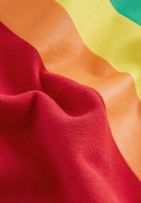 Textil anyag, amelyen piros, narancs, sárga és zöld hullámok láthatók, sima és puha textúrával, élénk színátmenettel.