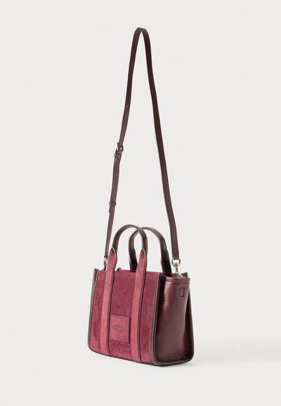 Lille maroon ruskind og læder handbag med to håndtag og en lang justerbar skulderrem, stående mod en hvid baggrund.