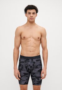 Schwarz-graue boxershorts im Camouflage-Muster mit einem breiten, elastischen Bund, der das Logo "UNDER" trägt, hergestellt aus einem glatten, dehnbaren Material.