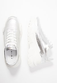 Baskets métalliques argentées avec une tige texturée, un design à lacets, une semelle en caoutchouc blanche et des détails perforés au niveau des orteils.