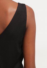 Top nero senza maniche con spalline larghe, realizzato in un tessuto morbido e liscio, con un design a V profonda sul retro.