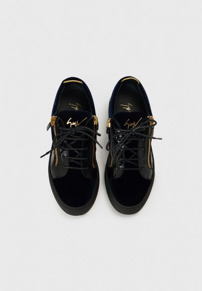 Czarne trampki z aksamitem w wykończeniu, złotymi zamkami błyskawicznymi i sznurowadłami. Posiadają gumową podeszwę i wytłoczone logo na języku.