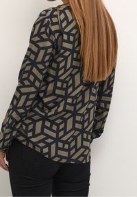 Chemise à manches longues avec un motif en vert foncé et bleu marine. Le tissu a une texture lisse, avec une coupe décontractée et un ourlet arrondi.