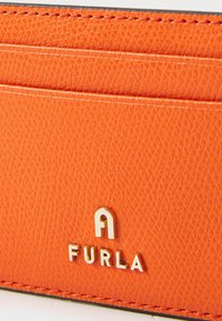 Oranž nahast kaarditasku, millel on kolm kaardipesa, tekstureeritud pind ja kuldse pressitud "FURLA" logo esiküljel.