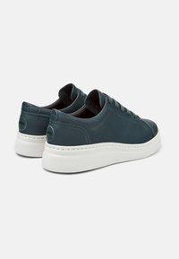 Sneakers in pelle verde scuro con suola piatta bianca, punta rotonda e lacci tonali. Presentano un logo circolare sul tallone.