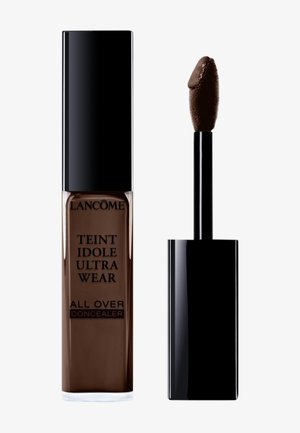 Lancôme Teint Idole Ultra Wear All Over Concealer in un tubo marrone scuro. Presenta un tappo nero elegante con un applicatore morbido attaccato.