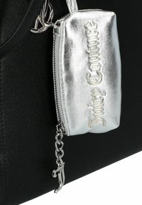 Kleine metallic zilveren ritszak met "Juicy Couture" gegraveerd, bevestigd aan een gestructureerde zwarte handtas met een zilveren ritscharme.