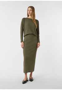 Sweter z dzianiny w oliwkowej zieleni o luźnym kroju, zestawiony z dopasowaną długą spódnicą. Oba elementy mają gładką fakturę i prosty design. Czarne baleriny.