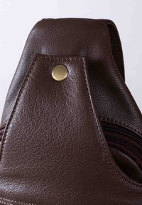 Brown leather bag detail featuring a textured finish, a triangular top with a brass snap, and a visible zipper along the edge.