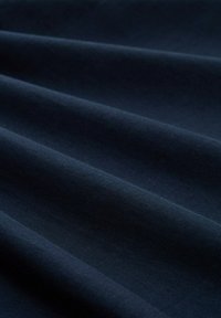 Marineblauwe stof met een gladde textuur, met zachte golven en plooien die diepte en schaduw creëren. Voornamelijk uniforme kleur.