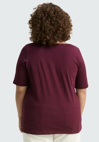 Haut bordeaux à manches courtes en tissu doux, avec un col rond et une coupe décontractée, présentant une texture lisse et sans motifs visibles.