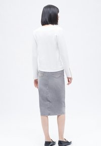 Top blanco de manga larga combinado con una falda lápiz de mezclilla gris. El conjunto presenta un corte clásico con una silueta recta y un diseño minimalista.