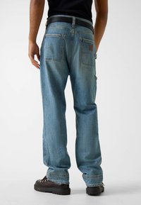 Jasnoniebieskie dżinsy o luźnym kroju, wyposażone w dwie tylne kieszenie i czarny pasek. Tkanina ma wyblakłą fakturę i delikatne przetarcia.