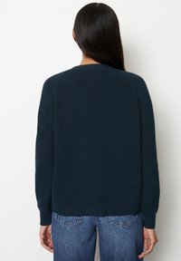 Mörkblå stickad tröja med raglanärmar, strukturerat mönster, rundad halsringning och ribbad nederkant. Stylerad med blå jeans.