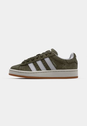 Des baskets en daim vert présentent trois rayures blanches, des lacets ronds, des perforations et une semelle intermédiaire blanche avec une semelle extérieure en caoutchouc légèrement brun.