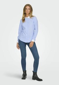 Lichtblauw gestreept overhemd met lange mouwen en een witte kraag, gecombineerd met donkerblauwe skinny jeans en zwarte enkellaarsjes met zilverkleurige hardware.