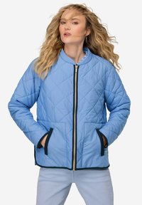 Světle modrá prošívaná bunda s vysokým límcem, zapínáním na zip, námořnickým lemováním a dvěma předními kapsami. Vyznačuje se hladkou texturou a diamantovým vzorem.
