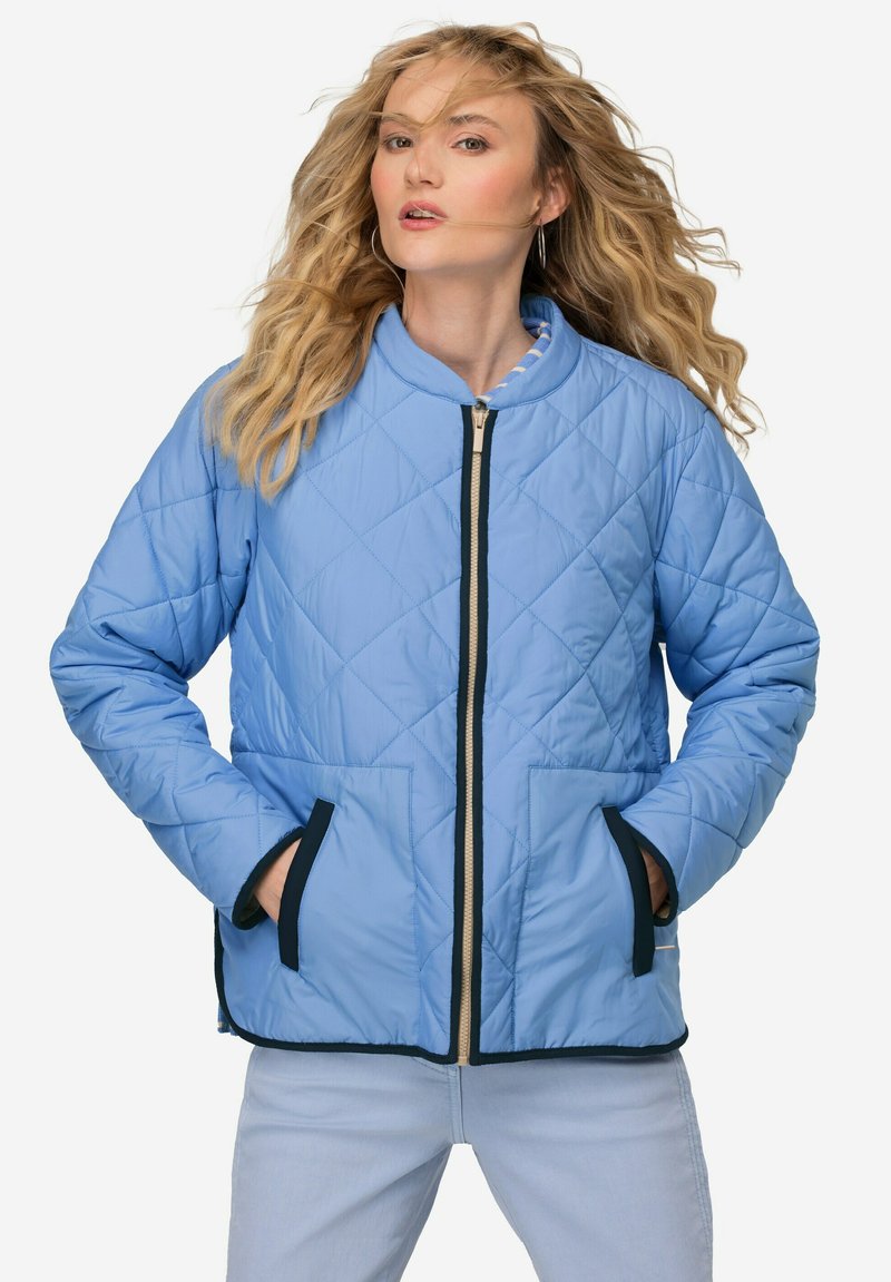 Světle modrá prošívaná bunda s vysokým límcem, zapínáním na zip, námořnickým lemováním a dvěma předními kapsami. Vyznačuje se hladkou texturou a diamantovým vzorem.