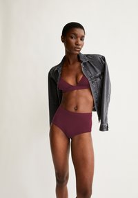 Bordeaux bikini-set met een triangulair bralette en hoge taille onderkleding, gecombineerd met een zwarte denim jacket. Gladde stof, minimalistisch ontwerp.