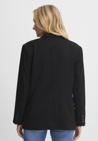 Črn blazer z oblikovanimi rameni, enim zadnjim razporkom in gumbnimi manšetami. Narejen iz gladkega blaga, ima prilega prilegajočo fit.
