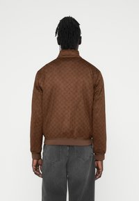 Καφέ μπουφάν bomber με υφή σε σχέδιο, ριμπ μανσέτες και τελείωμα, καθώς και όρθιο γιακά. Συνδυάζεται με σκούρα γκρί τζιν.