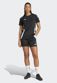 Top sportiv negru cu accente albe pe laterale, asortat cu pantaloni scurți negri. Caracteristici includ mâneci scurte, gât rotund și logo-ul Adidas pe piept.