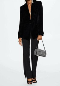 Czarna aksamitna marynarka z klapami, zapięciem na guziki i kieszeniami z przodu. Połączona z dopasowanymi czarnymi spodniami z bocznymi rozporkami i czarnymi sandałkami na wysokim obcasie.
