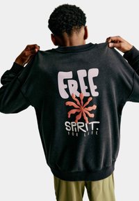 Černá mikina s kulatým výstřihem, s velkým bílým nápisem "FREE" a korálovým grafickým prvkem obklopeným slovy "SPIRIT FOR LIFE."