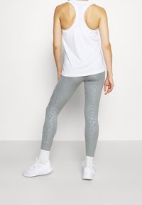 Collants gris clair avec un imprimé animalier discret, assortis à un débardeur blanc dos nageur et des chaussures de sport blanches. Matière lisse et extensible.