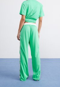 Green cotton short-sleeve top paired with matching wide-leg pants, featuring a white waistband and side stripes, shown from the back.