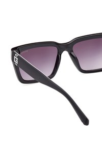 Svarta överdimensionerade solglasögon med gradientlila linser, med en glansig båge och en silverlogotyp på skalmarna.