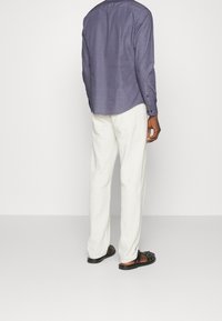 Langarmshirt in donkerpaars met een subtiel patroon, gecombineerd met witte broek en zwarte sandalen. Katoen met een gladde textuur.