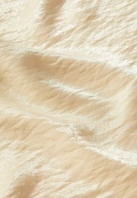 Tissu beige scintillant avec une surface texturée et ondulée. Le matériau semble brillant avec la lumière se reflétant sur son motif ondulé.