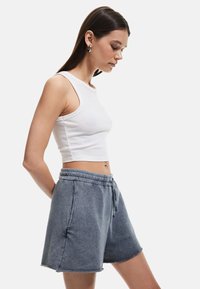 Valkoinen ribattu crop-top, jossa on leveät hihnat, yhdistetty harmaisiin naruhousuihin, joissa on etutaskut ja viimeistelemätön helma.