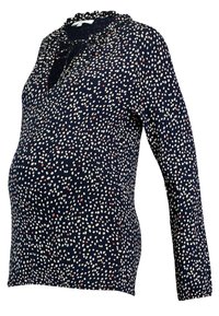 Graviditetslinne i marinblått tyg med vita och röda prickar, med runt halslinning och volangdetaljer samt långa ärmar.