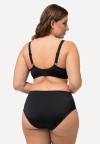Zwarte bh en hooggebode slipset met verstelbare straps, geschulpte details, een zachte textuur en een eenvoudig ontwerp.