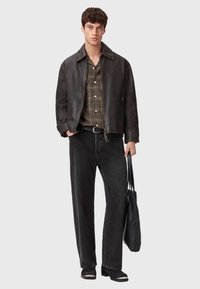 Giubbotto di pelle marrone, camicia a quadri, jeans neri, cintura nera, borsa nera. Vestibilità aderente, colletto con punte e bottoni a contrasto sulla camicia.