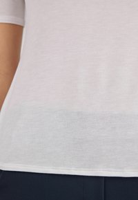 Kortærmet, lys grå t-shirt i blødt stof med en glat tekstur og en let gennemsigtig nederste sektion, med en lige kant.