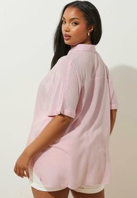 Ljusrosa kortärmad skjorta med krage, avslappnad passform, något genomskinligt tyg, uppvikta ärmar och rundad nederkant.