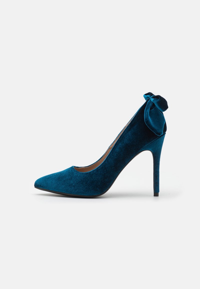 Teal velvet high-heeled pump with a pointed toe and a decorative bow on the back. Smooth texture and slender, stiletto heel design.